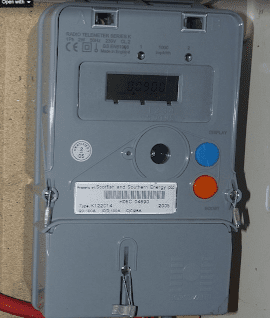 A close-up photograph of a grey radio teleswitch electricity meter mounted on a board. The meter has a digital display showing energy usage, multiple buttons for control (blue and orange), and security seals on the casing. A label below the display indicates it is associated with Scottish and Southern Energy. Electrical wiring is connected at the bottom.